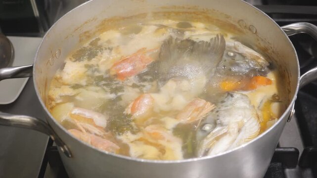 Sea bass and shrimp broth boiling in pot with herbs, traditional seafood stock