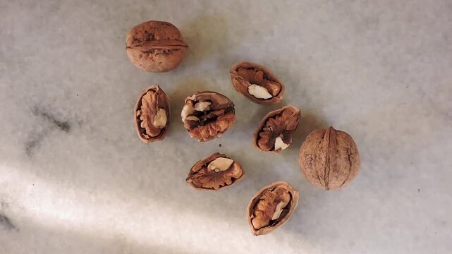 several walnuts on a marble surface, some in their shells and others cracked open to reveal the kernel inside