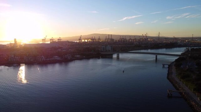 Shipping port and industrial dock supporting import export and global trade. Cargo ships, trains, and semi trucks move goods through a major harbor at sunset in Los Angeles California.