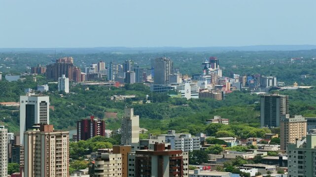 Drone video showcasing Foz do Igua&ccedil;u skyline, lush greenery, and Ciudad del Este in the background, divided by the majestic Parana River, under clear blue skies. No people visible.