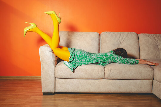 Woman in colorful clothing lying face down on sofa in surreal humorous scene