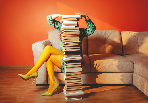 Person with yellow tights reading on sofa behind large stack of books