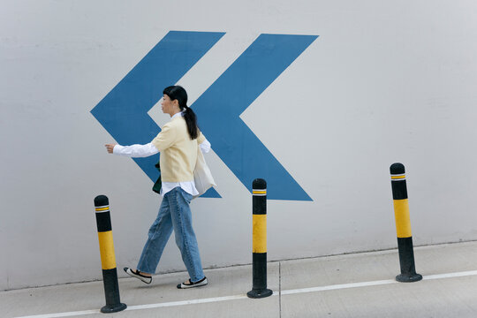 Woman walking in urban setting in casual outfit beside graphic arrow