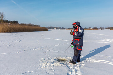 An Ice fisherman uses a winter spinning rod and reel to catch perch or pike in a hole on the frozen surface of a river.