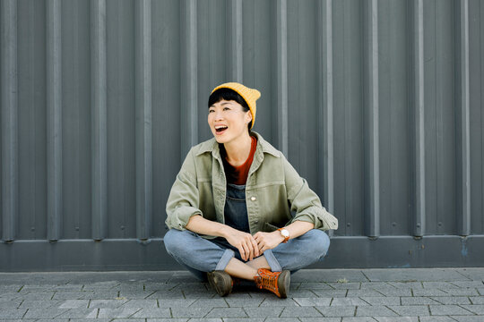 Laughing individual in hipster outfit sitting outdoors urban setting