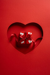 Obraz premium A vertical romantic Valentine scene features a red gift box with white heart patterns framed by a heart cutout. Perfect for love, romance, greeting cards, and Valentine celebrations