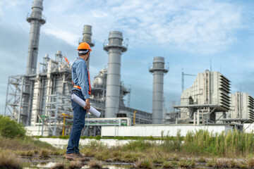 Engineer holding blueprint and observing industrial power plant structure during field inspection....