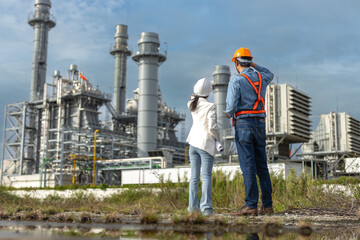Two engineers wearing safety helmets inspecting power plant infrastructure at construction site,...