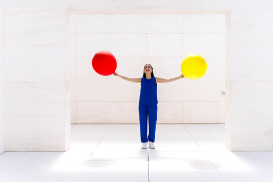 Woman in blue outfit holding red and yellow balloons outdoors