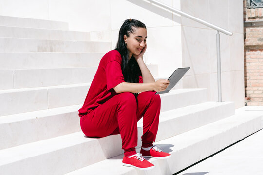 Woman in red outfit sitting on outdoor stairs using tablet