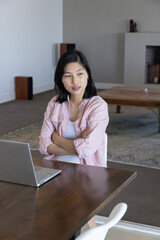 Naklejka premium Asian korean woman sitting at table typing on silver laptop in home workspace featuring rug