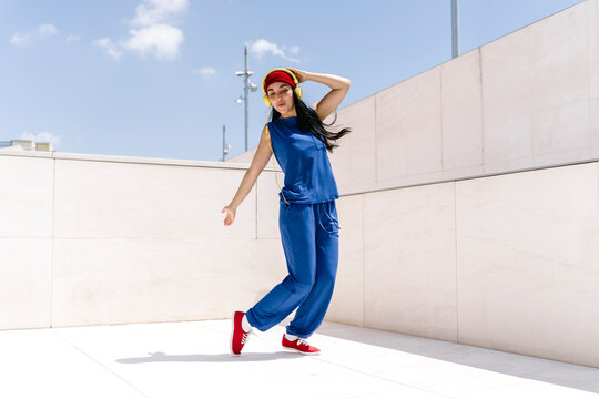 Woman dancing outdoors in blue outfit with red shoes and red hat