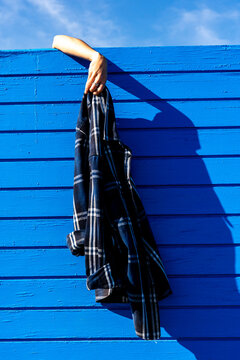 Hand holding plaid shirt over bright blue urban wall with strong shadow