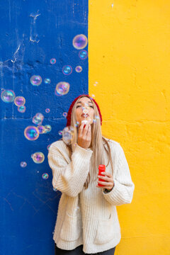 Woman blowing bubbles in front of a colorful wall outdoors