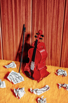 Toy violin and bow with crumpled sheet music on orange surface in retro setting