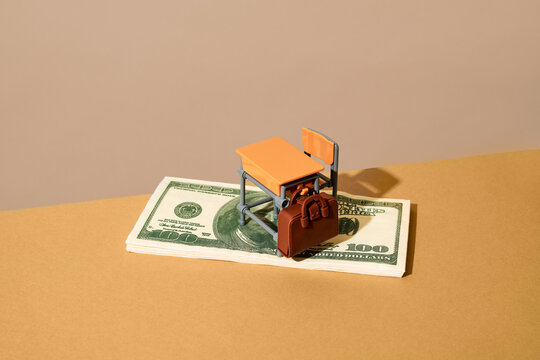 Toy school desk and chair on stack of money representing education spending