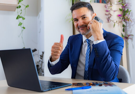 Young entrepreneur looking very pleased, nodding his head while talking on the phone and working on his laptop.