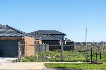 Obraz premium Suburban residential area with newly built houses beside a fenced vacant lot. Undeveloped land reflect ongoing housing development and future construction within outer metropolitan estate in Melbourne