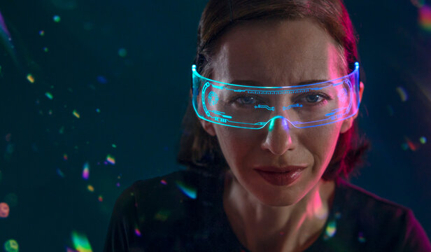 Woman wearing glowing virtual reality glasses indoors