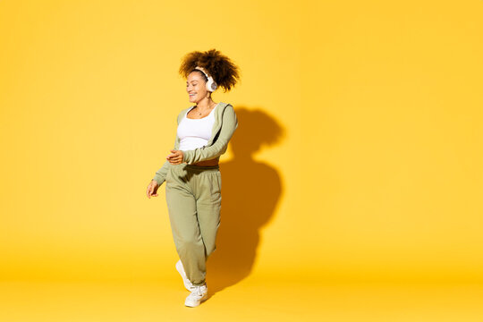Cheerful woman with wireless headphones dancing in front of yellow background