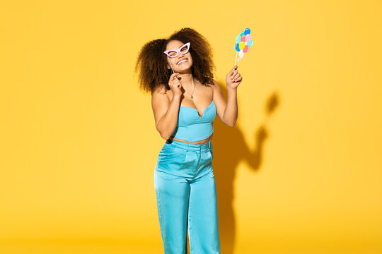 Cheerful young woman holding balloon prop against yellow background