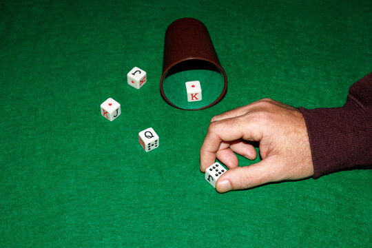 Hand playing dice game on green mat with cup and dice close up