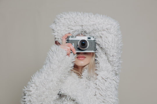 Stylish woman in fur coat taking photo with vintage camera indoors