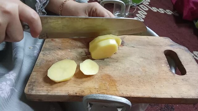 Realistic video of slicing potato on wooden cutting board with clear chopping sound. Everyday kitchen activity for food preparation and material interaction.