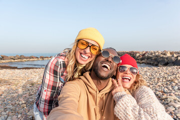 Group of Multiracial diverse friends in sunglasses laughing and taking selfie on pebble beach