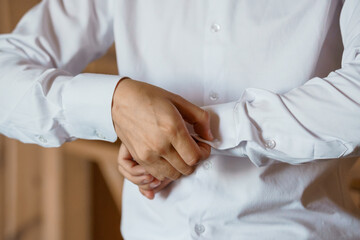 Obraz premium Man in White Dress Shirt Buttoning Cufflinks, Close-Up Hands, Formal Attire, Elegant Style, Neutral Background