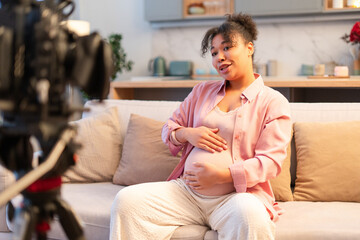 Obraz premium Beautiful pregnant African American woman embracing pregnant belly, blogger recording video