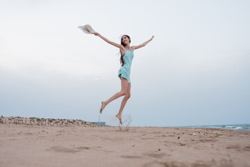 Obraz premium Young woman happily jumping barefoot on a sandy beach during summer vacation with copy space