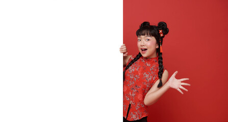 Asian child presenting blank banner for Chinese New Year promotion young girl peeking and gesturing with excitement to showcase copy space festive marketing holiday celebration tradition and joy.