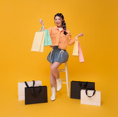 Shopping lifestyle promotion Asian woman holding colorful shopping bags while sitting on stool to represent retail happiness consumer excitement seasonal sale modern shopping experience.