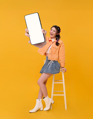 Smartphone app promotion Asian woman holding blank screen mobile phone showing while sitting on stool to present digital marketing mobile advertising online engagement.