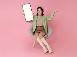 Smartphone app promotion concept with Asian woman holding blank screen mobile phone while sitting on chair to present digital marketing online advertising social media engagement.