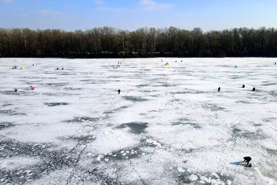 icy background in winter. Fishermen are fishing on beautiful blue ice, frozen river, lake in winter