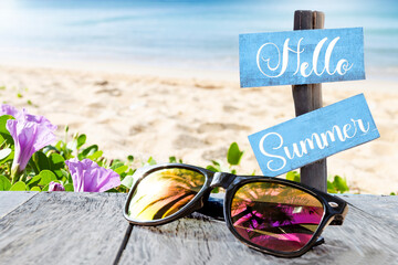 Hello summer sign with sunglasses on wooden table over blurred tropical beach background, summer season, outdoor day light