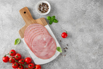 Delicious ham cut into round slices on a cutting board with spices, cherry tomatoes and basil leaves on a gray stone background. Top view. © irina2511
