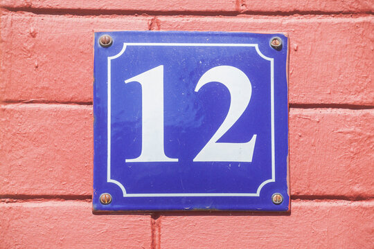 Blaues Hausnummernschild Nr. 12 auf rosa Hauswand, Deutschland