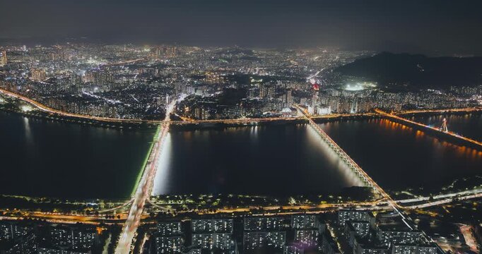 Aerial perspective captures a bustling city at night with bright lights reflecting on the water and bridges linking urban sections. Time-lapse, Seoul, South Korea