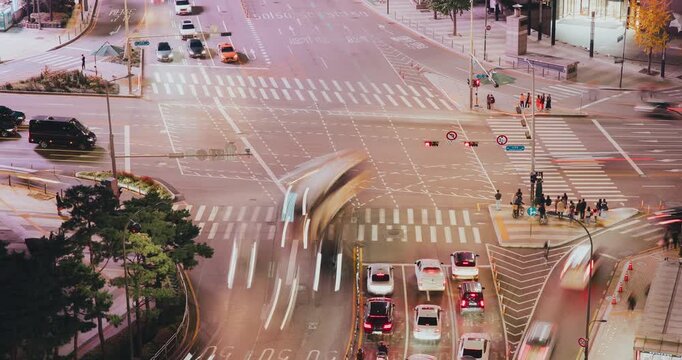 An urban intersection captures the flow of vehicles and pedestrians navigating crosswalks under city lights, highlighting movement and activity. Time-lapse, Seoul, South Korea