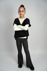 Full-length portrait of a young girl wearing stylish glasses, a white long-sleeve shirt, a black...