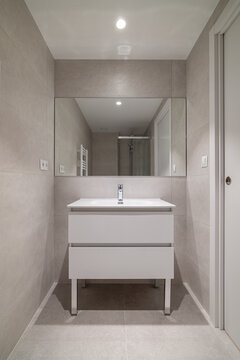 Modern bathroom interior with a sleek white vanity, large mirror, and neutral tile walls. Bright lighting enhances the clean design.