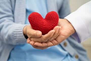 Doctor giving a red heart to senior patient in hospital.