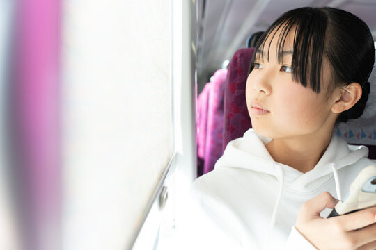 電車の窓から外を見る10代の女性