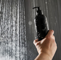 Hand holding black shampoo pump bottle in the shower