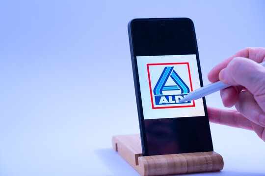 Hand tapping stylus on smartphone showing aldi logo, representing online shopping and digital access
