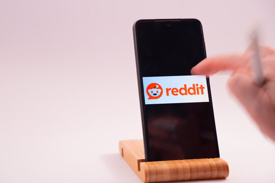 Hand tapping reddit logo on a mobile phone display, illustrating social media interaction