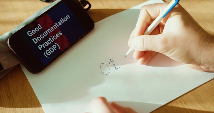 Close-up of a hand correcting a written date by striking through the error and adding a side note with justification, while &ldquo;Good Documentation Practices (GDP)&rdquo; is shown on a smartphone. Ideal for pha